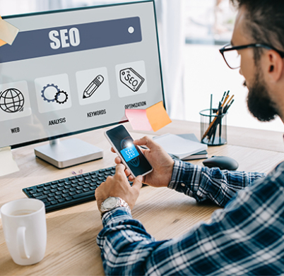 handsome young seo manager using smartphone and computer at workplace